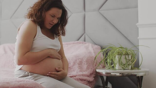 Expectant mother suffering from pregnant pain. Pregnant woman feeling ache lying on a bad.  Pregnant adult woman feels pain  expecting childbirth. Pregnant woman cannot fall asleep from abdominal pain