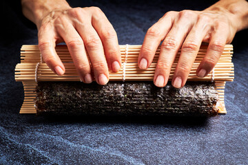 Female chef preparing a roll with rice and nori for a delicious sushi. Asian food concept