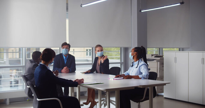 International team of business colleagues in protective masks working together in office boardroom
