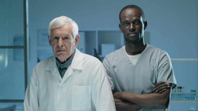 Portrait of senior Caucasian scientist and his young Afro-American male colleague standing together in lab and posing for camera