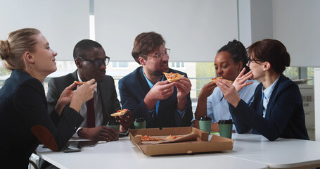 Young international business team having lunch break in office eating pizza together