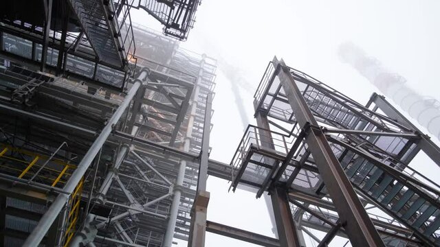 Movement under metal structures. Epic industrial landscape. Chimney obscured by fog in the background.