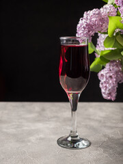 Full glass of red wine on a gray concrete table. Table decoration - lilac with purple flowers and green leaves. Aperitif concept. Dark background. Side view