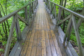 A small bridge made of wooden boards with handrails across a narrow stream in a city park