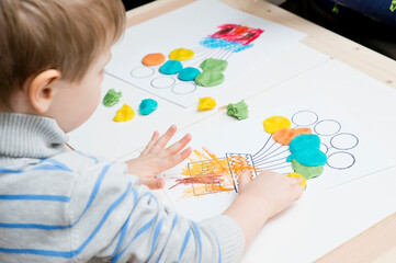 Two pairs of children hands coloring drawing of house with balloons with colored wax crayons. exercise for hand-eye coordination, stimulate imagination, creativity, develop fine motoric skills.