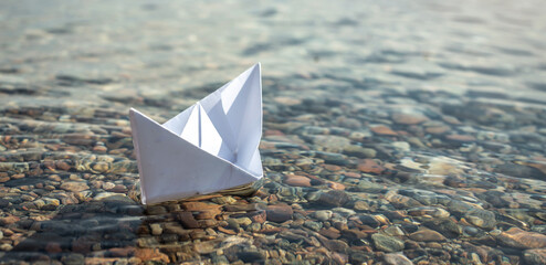White paper boat in the clear water of the sea with a stony bottom