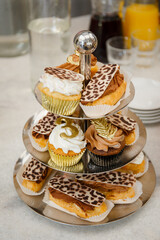 Festive table with sweet treats in the form of cakes and eclairs with custard and chocolate cream. Birthday gilded cupcakes