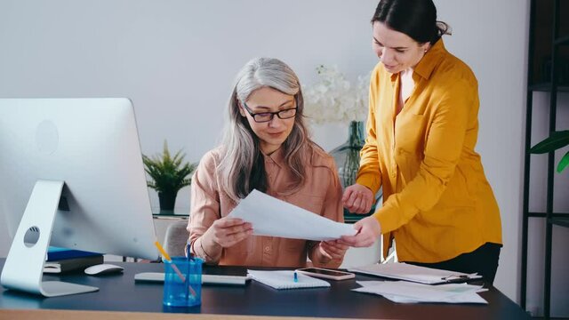 Team: two successful businesswoman sitting at desk having fun at work.