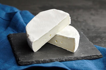 Brie cheese head on black slate board on blue linen napkin over dark background