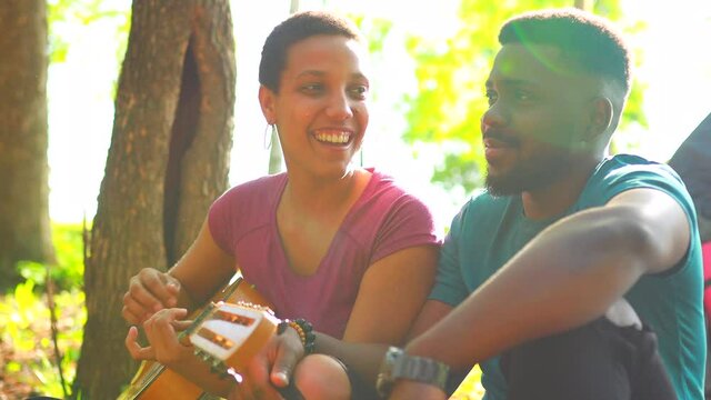 two happy african american people in love spending time outdoors in camp playing guitar and singing