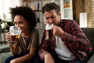 Boyfriend and girlfriend drinking beer at home. Happy couple watching sports game on tv..