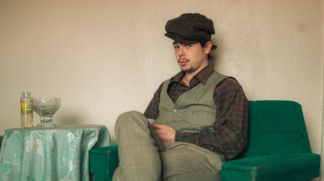 man in vintage suit is sitting on sofa and holding coffee cup. an old house. old colors. vintage background