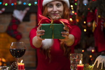 Pretty woman in Santa Claus hat near fireplace