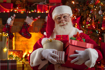 Santa Claus with gift box presents near fireplace and Christmas tree. Wooden house, New Year's...