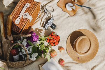 Summer picnic with food and drink in wicker basket, book and female straw hat.