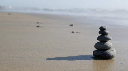 Rock balancing on ocean beach, stones stacking by sea water waves. Pyramid of pebbles on sandy shore. Stable pile or heap in soft focus with bokeh, close up. Seamless looped cinemagraph. Zen balance. - obrazy, fototapety, plakaty