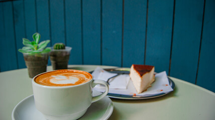 A cup of cappuccino, a slice of cheesecake on a beautiful table. A beautiful design with distant flowers.