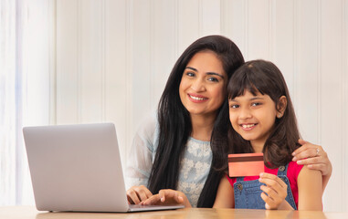 A YOUNG WOMAN AND DAUGHTER LOOKING AT CAMERA WHILE DOING ONLINE TRANSACTION	