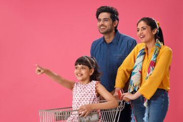 A YOUNG CHILD POINTING AWAY WHILE HER PARENTS HAPPILY LOOK WHILE SHOPPING	