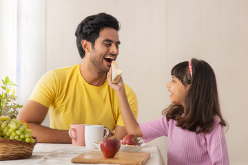 A YOUNG CHILD HAPPILY GIVING SANDWICH TO HER FATHER	