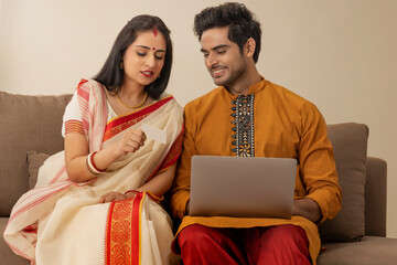 A HAPPY COUPLE IN TRADITIONAL CLOTHING LOOKING AT EACH OTHER WHILE DOING ONLINE TRANSACTION	 - obrazy, fototapety, plakaty