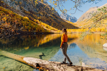 Fototapeta na wymiar Woman at crystal lake in the autumnal mountains. Mountain lake and traveller