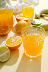 Vertical image.Closeup of glass of fruity beverage, limes,oranges on the yellow table