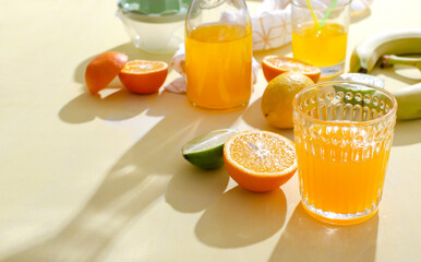 Glass and bottle of fruity summer beverage, slices of oranges, limes,lemon on the yellow table.Empty space