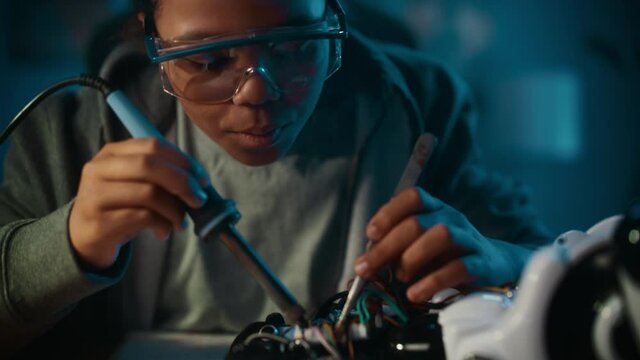 Young Teenage Multiethnic Schoolgirl is Studying Electronics and Soldering Wires and Circuit Boards in Her Science Hobby Robotics Project. Girl is Working on a Robot in Her Room. Education Concept.