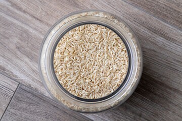 A top down close up portrait of a glass pot full of rice standing on a wooden table. The uncooked and raw food is ready to be boiled and cooked as a side dish for a delicious meal.
