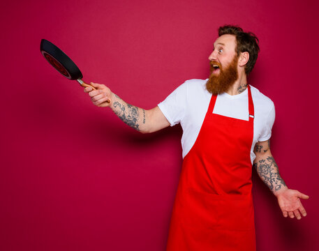 Happy chef with beard and red apron cooks with pan