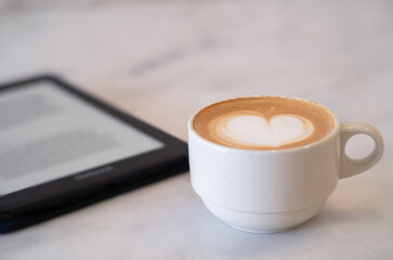 Close-up of Hot coffee latte with latte art milk foam in cup or mug with ebook reader tablet on desk in coffee shop at the cafe business work concept