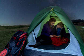 Woman and boy in a tent at night reading a book