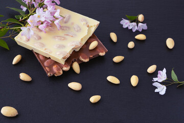 a bar of milk and a bar of white chocolate with almonds and a sprig with flowers of a decorative almond bush