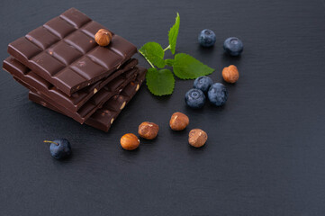 chocolate bars with hazelnuts, next to blueberries and hazelnut itself