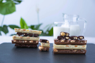 broken bars of black, white and milk chocolate with nuts, a jug of milk