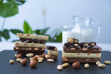 broken bars of black, white and milk chocolate with nuts, a jug of milk and sprinkled nuts