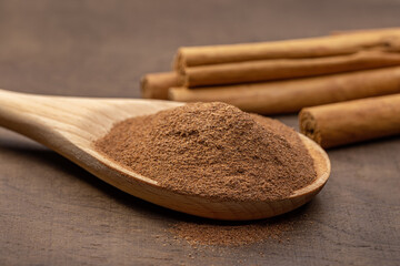 Wooden spoon with crushed cinnamon, rolls of natural cinnamon on a brown wooden background. Close-up, copy space.