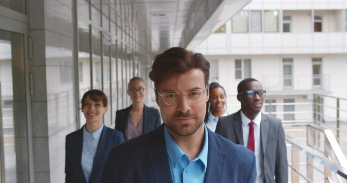 Successful team of diverse business people confidently striding along office building