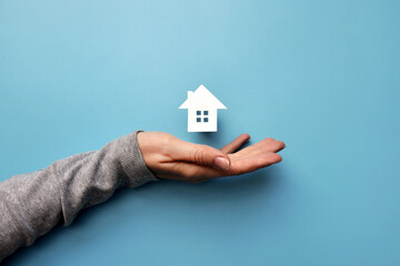 A man holds a paper house in his hand. The symbol of the purchase of housing