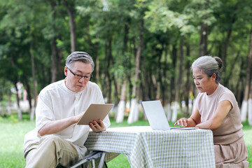 Fototapeta premium Happy old couple use computer to surf the Internet outdoors