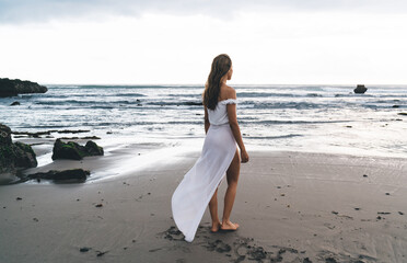 Fototapeta na wymiar Anonymous barefooted female tourist enjoying breeze on sandy beach