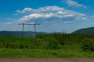 Fototapeta na wymiar High power lines in a green area against a blue sky with white clouds.