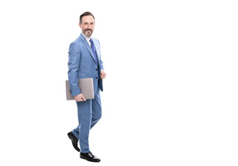 Fototapeta premium happy grizzled boss in suit full length walking with laptop isolated on white copy space, freelancer