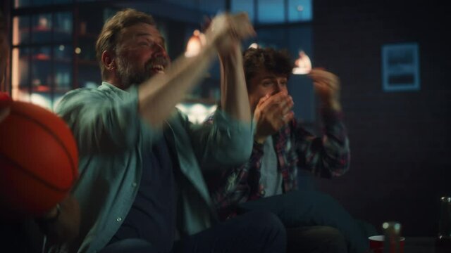 At Home Three Joyful Basketball Fans Sitting on a Couch Watch Game on TV, Celebrate Victory when Sports Team Wins. Group of Friends Cheer When Favourites Play on Championship. Portrait Shot