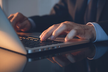 Businessman hand typing on laptop computer on office table with sunlight, closeup