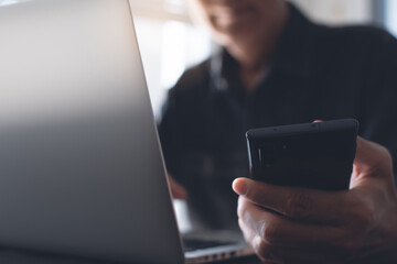 Closeup of man working on laptop computer and using mobile phone at home, telecommuting, work from home