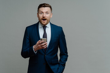 Surprised businessman in suit reading unexpected news on mobile phone