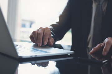 Businessman in black suit working on laptop computer and using mobile smart phone at modern office