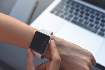 Woman checking time on her smart watch during working on laptop computer